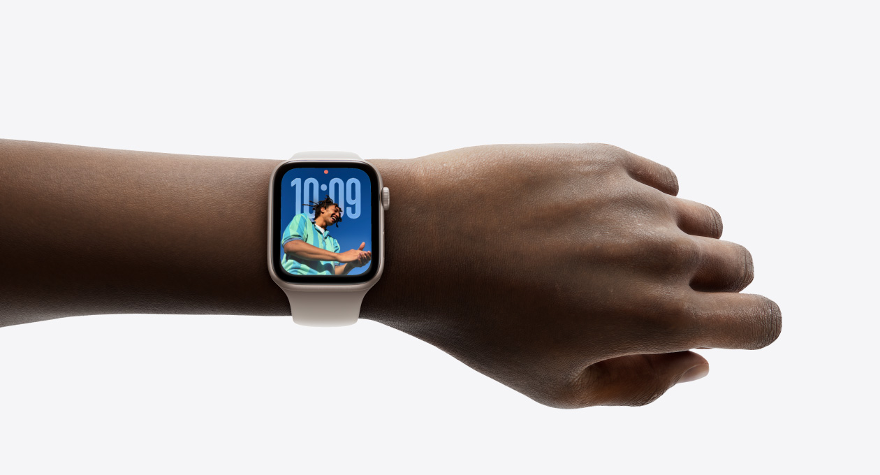 صورة مقرّبة لساعة Apple Watch باللون الفضي مع حزام مطاطي على معصم، تُظهر تطبيق الوقت بتصميم Liquid Glass الجديد