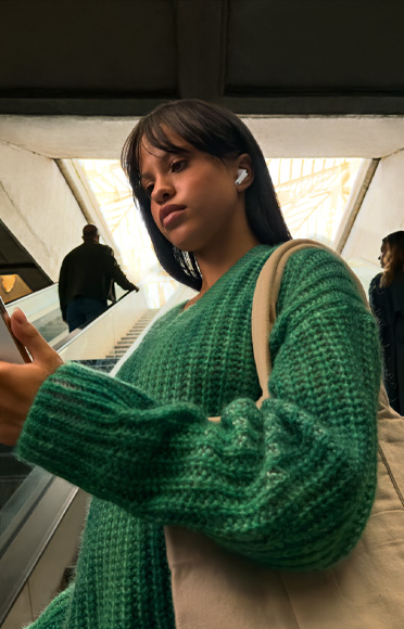 Į „iPhone“ žiūrintis žmogus su „AirPods Pro 3“